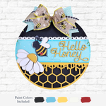 The Rustic Rhode DIY Honey Bee Door Hanger is a round, laser-cut wood sign with a bee, daisies, honeycomb pattern, and bee-print bow. It says Hello Honey in yellow script on blue—perfect for paint-your-own projects.