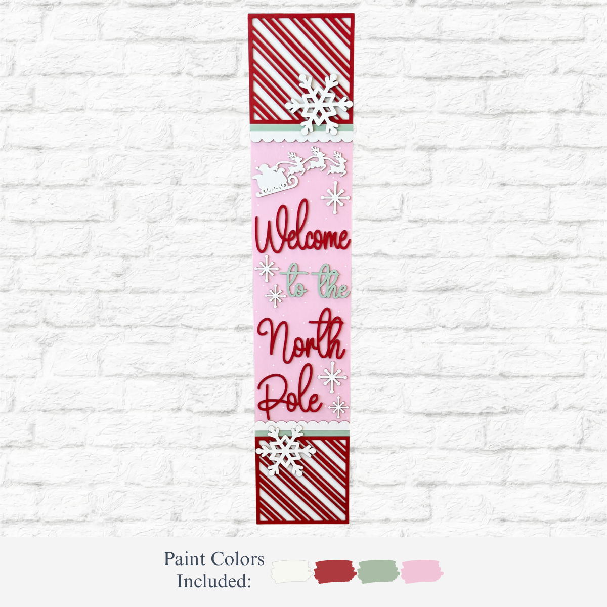 The Rustic Rhode's DIY North Pole Porch Leaner features “Welcome to the North Pole” text, Santa’s sleigh, and festive colors—perfect Christmas porch decor for your white brick wall.