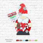 The Rustic Rhode's DIY North Pole Santa Gnome features a red-hatted gnome with holiday signs, gifts, treats, and snowflakes—ideal for festive home décor. Shown with red, brown, beige, green, blue, white & pink on a white brick background.