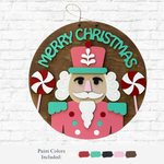 The Rustic Rhode’s DIY Nutcracker Door Hanger is a round, laser-cut wood sign with a colorful nutcracker, candy canes, and “Merry Christmas” in teal—perfect holiday décor. Includes paint samples: white, green, red, teal, pink & brown.