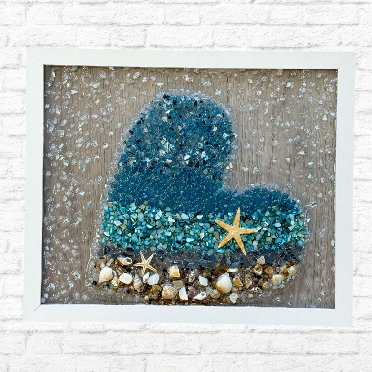 The Rustic Rhode DIY Ocean Heart Sea Glass Frame features blue and clear glass, shells, and starfish on a textured background, adding ocean-inspired charm to your space. Perfect coastal decor for any room.