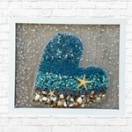 The Rustic Rhode DIY Ocean Heart Sea Glass Frame features blue and clear glass, shells, and starfish on a textured background, adding ocean-inspired charm to your space. Perfect coastal decor for any room.