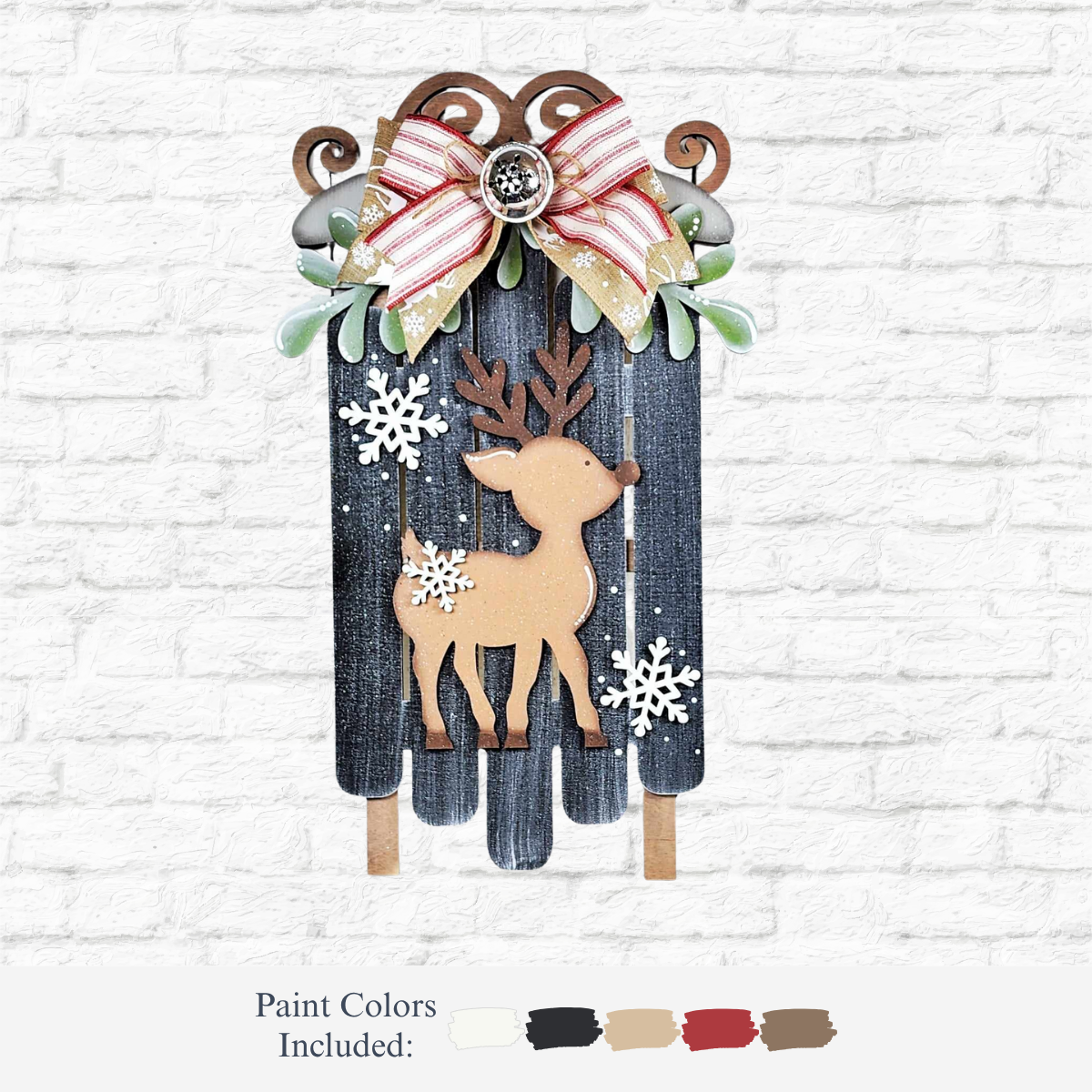 The Rustic Rhode’s DIY Oh Deer Sled Door Hanger is a decorative wooden sled with a cutout reindeer, snowflake accents, green leaves, and a red-and-white striped bow—perfect holiday décor for your white brick wall. Paint colors shown below the image.
