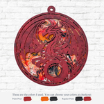 The Rustic Rhode’s DIY Paint Pour-Dragon kit features a circular ornament with a cutout dragon, painted in red, black, orange, and white using the pour technique. Paint color options are displayed below against a white brick wall background.