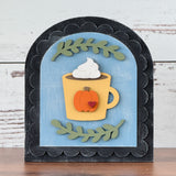 Decorative wall art with a pumpkin-themed mug and whipped cream on a wooden surface.