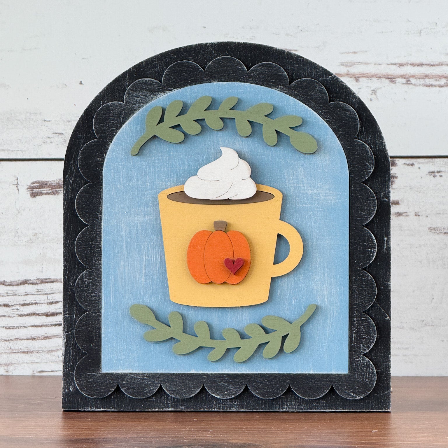 Decorative wall art with a pumpkin-themed mug and whipped cream on a wooden surface.
