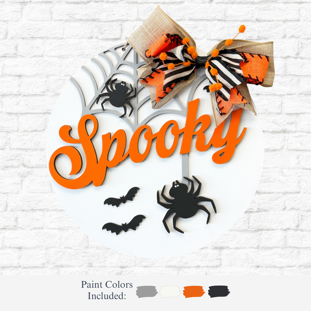 The Rustic Rhode’s DIY Spooky Halloween Door Hanger features Spooky in orange, bats, a spider, web, and bow on a round white sign—perfect for Halloween décor! Paint colors: gray, black, white, orange.