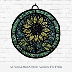 The Rustic Rhode DIY Sunflower Faux Suncatcher—a round panel with a bright yellow sunflower, green leaves, and black frame—hangs on a white brick wall. Text reads: “All Paint & Stain Options Available For Frame.”.
