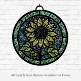 The Rustic Rhode DIY Sunflower Faux Suncatcher—a round panel with a bright yellow sunflower, green leaves, and black frame—hangs on a white brick wall. Text reads: “All Paint & Stain Options Available For Frame.”.