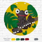 The therusticrhode DIY Tree Frog Kids Kit features a circular wooden base with a black frog with big eyes and a red smile on a branch with green leaves, set on a yellow background. This fun craft kit helps boost fine motor skills. Paint colors shown below.