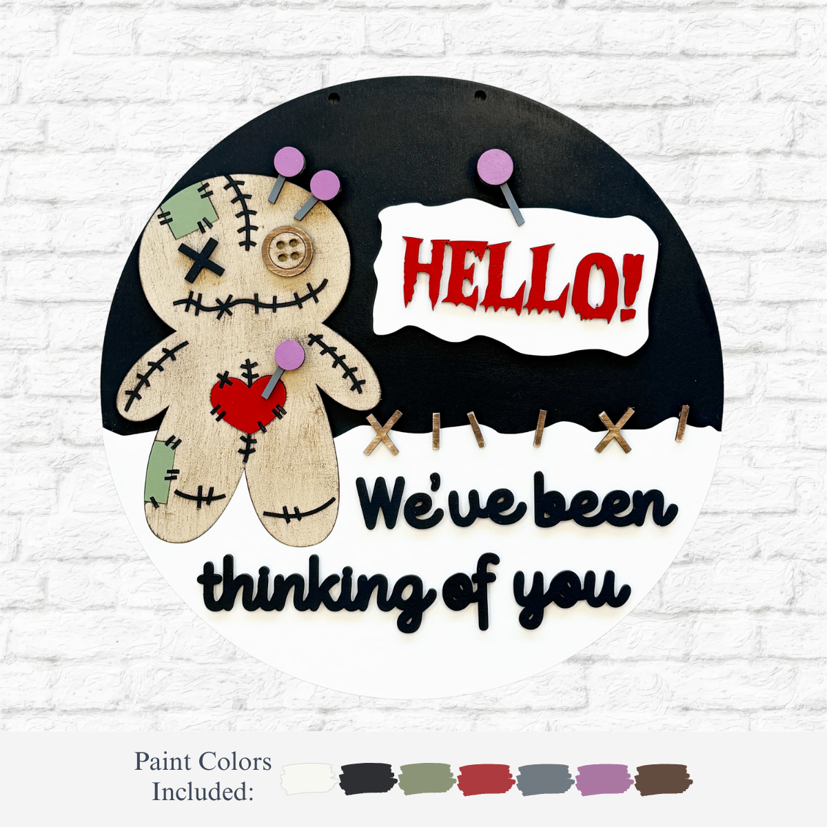 The Rustic Rhode’s DIY Voodoo Doll Door Hanger is a round sign with a stitched doll, red HELLO! speech bubble, and “We’ve been thinking of you” in black, plus paint color samples on a white brick background.