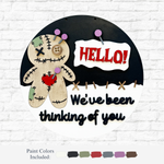 The Rustic Rhode’s DIY Voodoo Doll Door Hanger is a round sign with a stitched doll, red HELLO! speech bubble, and “We’ve been thinking of you” in black, plus paint color samples on a white brick background.