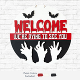 The Rustic Rhode’s DIY We’re Dying To See You Door Hanger features red WELCOME, white WERE DYING TO SEE YOU, black bats and zombie hands, plus red, white, and black paint swatches—perfect for a spooky Halloween door decoration.