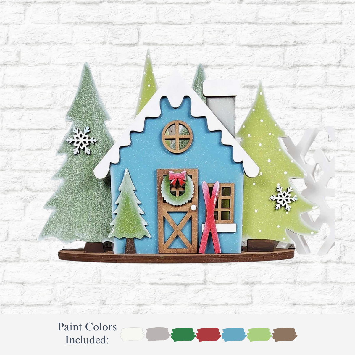 The Rustic Rhode's DIY Welcome Winter Mantle Sign features a small blue wooden house with a snowy roof, pine trees, snowflakes, wreath, and red skis for a cozy winter scene. Paint colors are shown below.