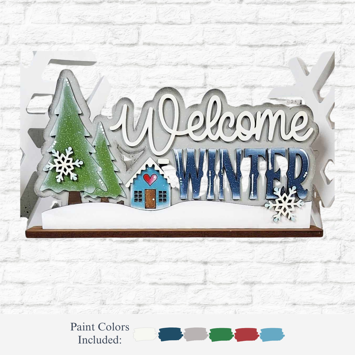 The Rustic Rhode DIY Welcome Winter Word Art features a green pine tree, small house, snowflakes, and "Welcome Winter" in white and blue on a white brick background—perfect for personalized home decor projects. Paint colors shown below.
