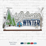 The Rustic Rhode DIY Welcome Winter Word Art features a green pine tree, small house, snowflakes, and "Welcome Winter" in white and blue on a white brick background—perfect for personalized home decor projects. Paint colors shown below.