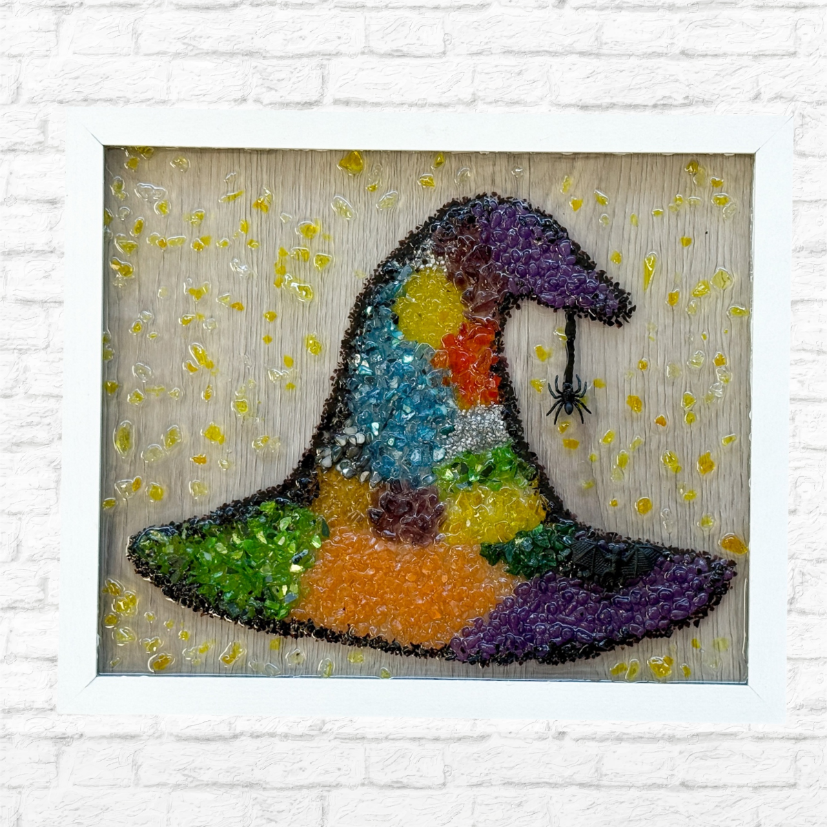 The Rustic Rhode DIY Witchs Hat Sea Glass Frame features a colorful witch hat and black spider in glass on a light wood background, accented with yellow drops—perfect Halloween decor for your home.