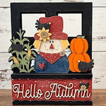 The Rustic Rhode’s DIY Interchangeable Window Frame features a decorative sign with a cheerful scarecrow, sunflowers, corn, pumpkins, blackbirds, and “Hello Autumn” in white cursive on a red background.