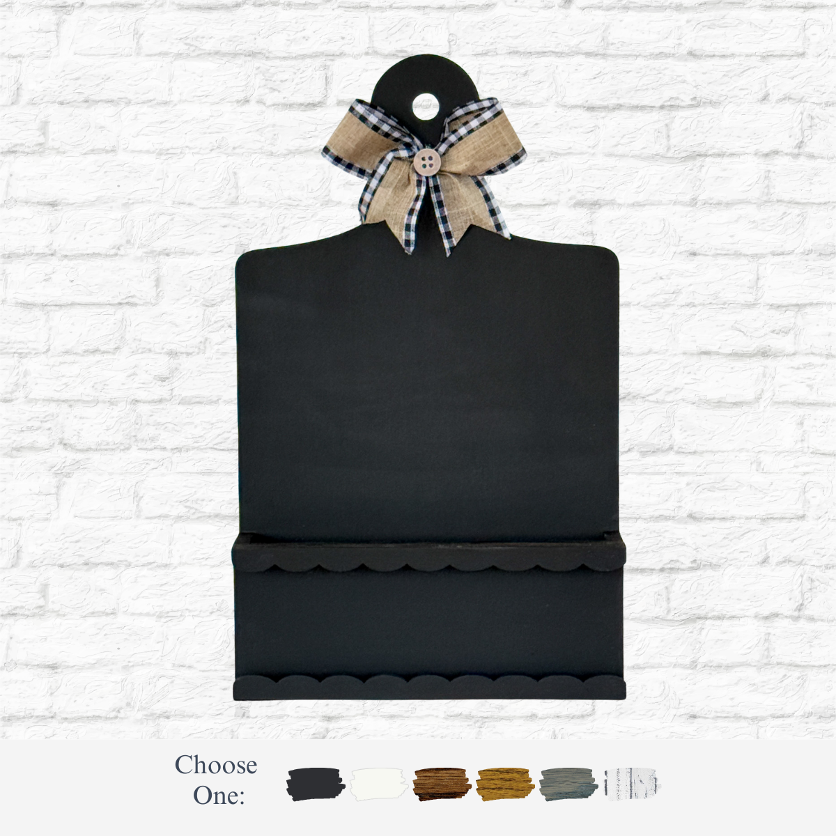 The Rustic Rhodes DIY Interchangeable Breadboard Frame hangs on a white brick wall, featuring black with a scalloped edge, small shelf, and burlap & black gingham ribbon bow. Color options are displayed at the bottom.