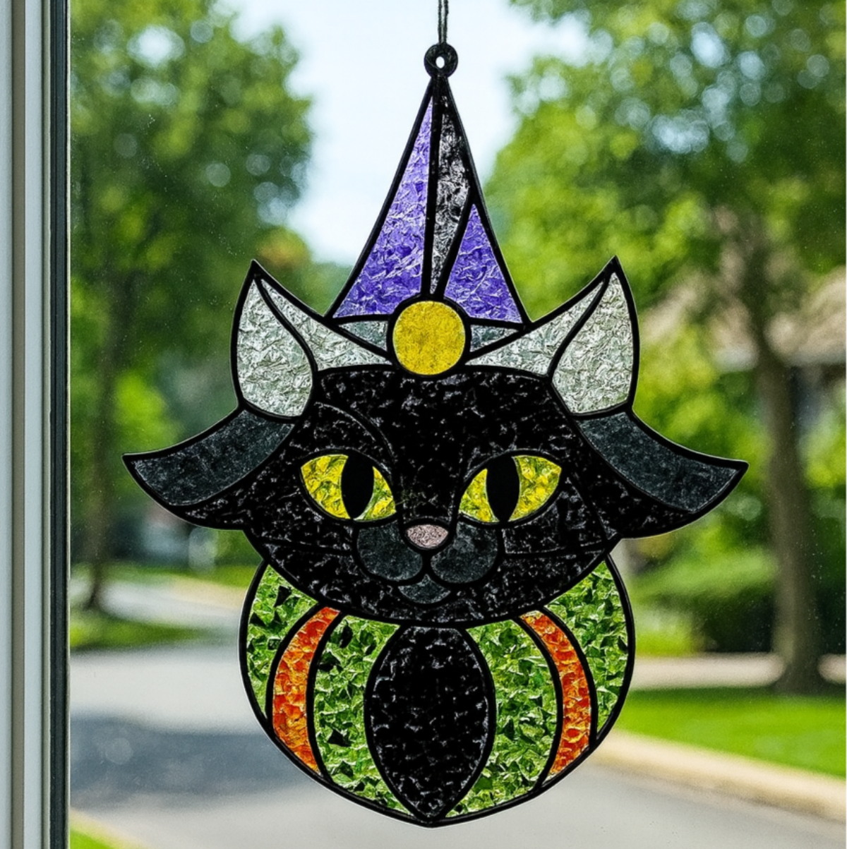 Stained glass cat decoration hanging on a door with a view of trees and road outside.