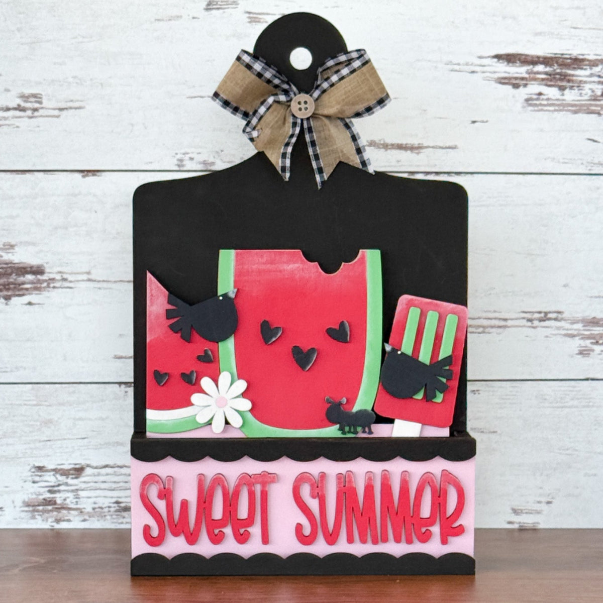 The Rustic Rhode DIY Watermelon Summer 2 Piece Insert features watermelon slices, black birds, ants, flowers, and a red spatula on a black board with plaid bow. “SWEET SUMMER” in bold pink letters accents the decorative sign.
