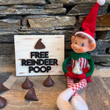 The Rustic Rhode DIY Elf Prop Kit features a smiling Christmas elf doll sitting by a "Free Reindeer Poop" sign with chocolate candy, plus handcrafted elf props and chocolates—perfect for festive holiday displays.
