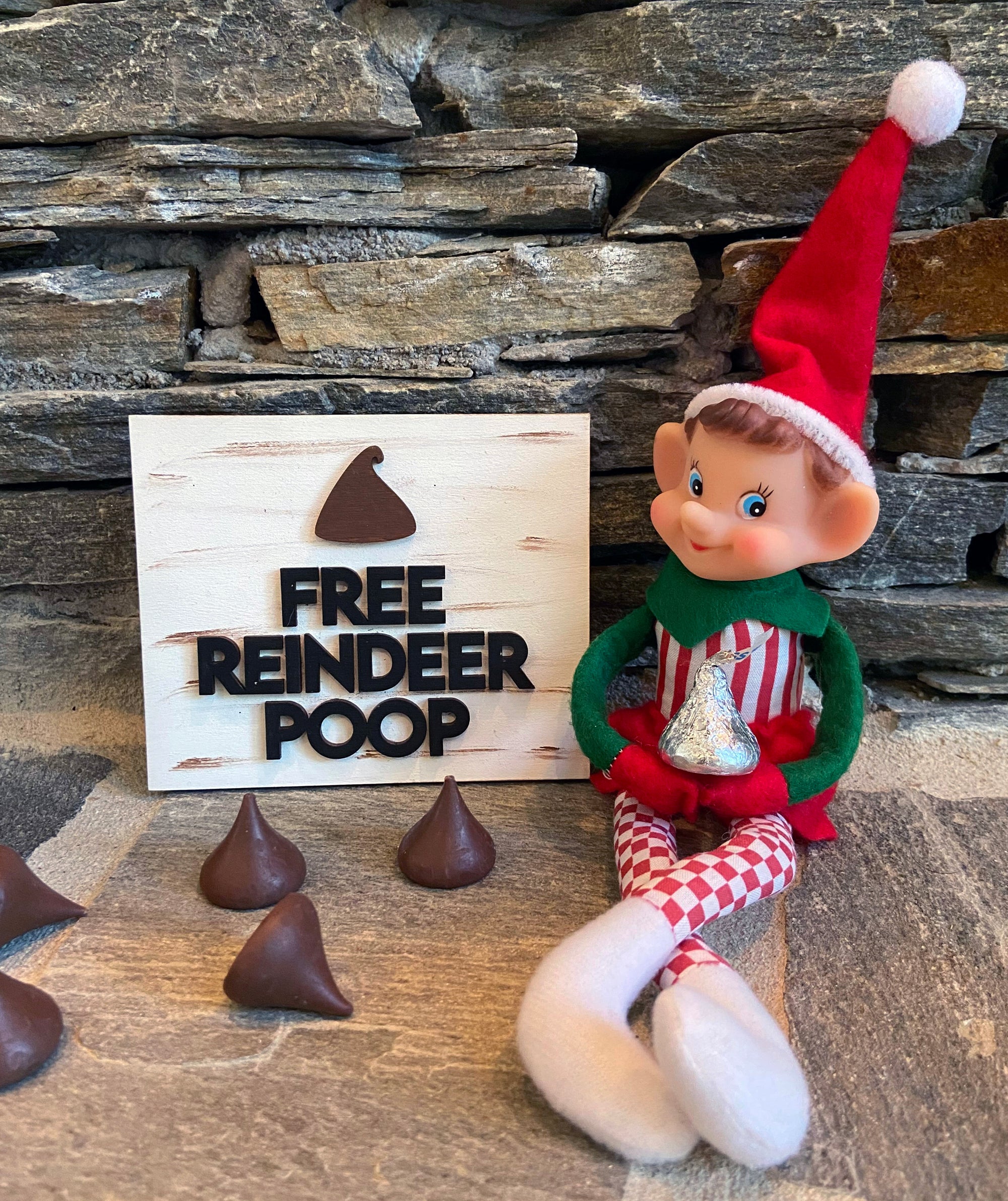 The Rustic Rhode DIY Elf Prop Kit features a smiling Christmas elf doll sitting by a "Free Reindeer Poop" sign with chocolate candy, plus handcrafted elf props and chocolates—perfect for festive holiday displays.