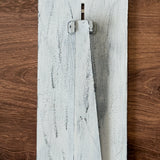 The Rustic Rhode DIY Interchangeable Farmhouse Frame is a distressed white wood piece with a triangular stand, resting on brown wood—ideal for personalized home decor.
