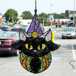 The Rustic Rhode's Autumn Magic Suncatchers Workshop features a black cat suncatcher with yellow eyes and a purple wizard hat—perfect for Halloween crafting fun, seen hanging in a window with parked cars outside.