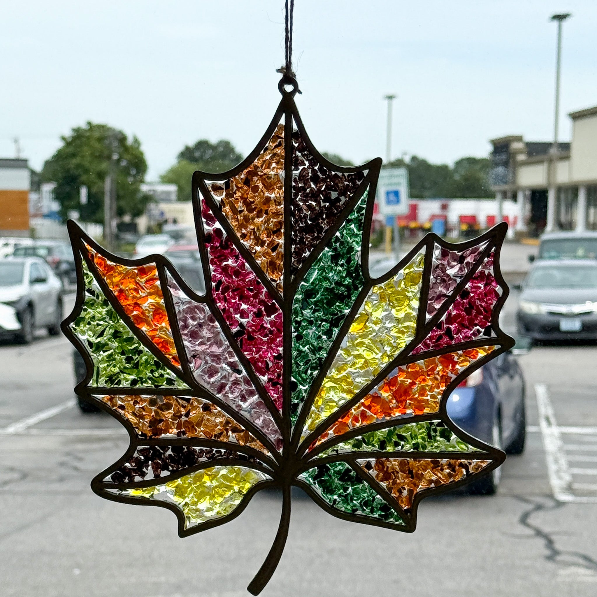 The Rustic Rhode's Autumn Magic Suncatchers Workshop features a stained glass maple leaf in red, yellow, green, and orange—perfect for fall crafts and gorgeous in a window overlooking autumn scenery.