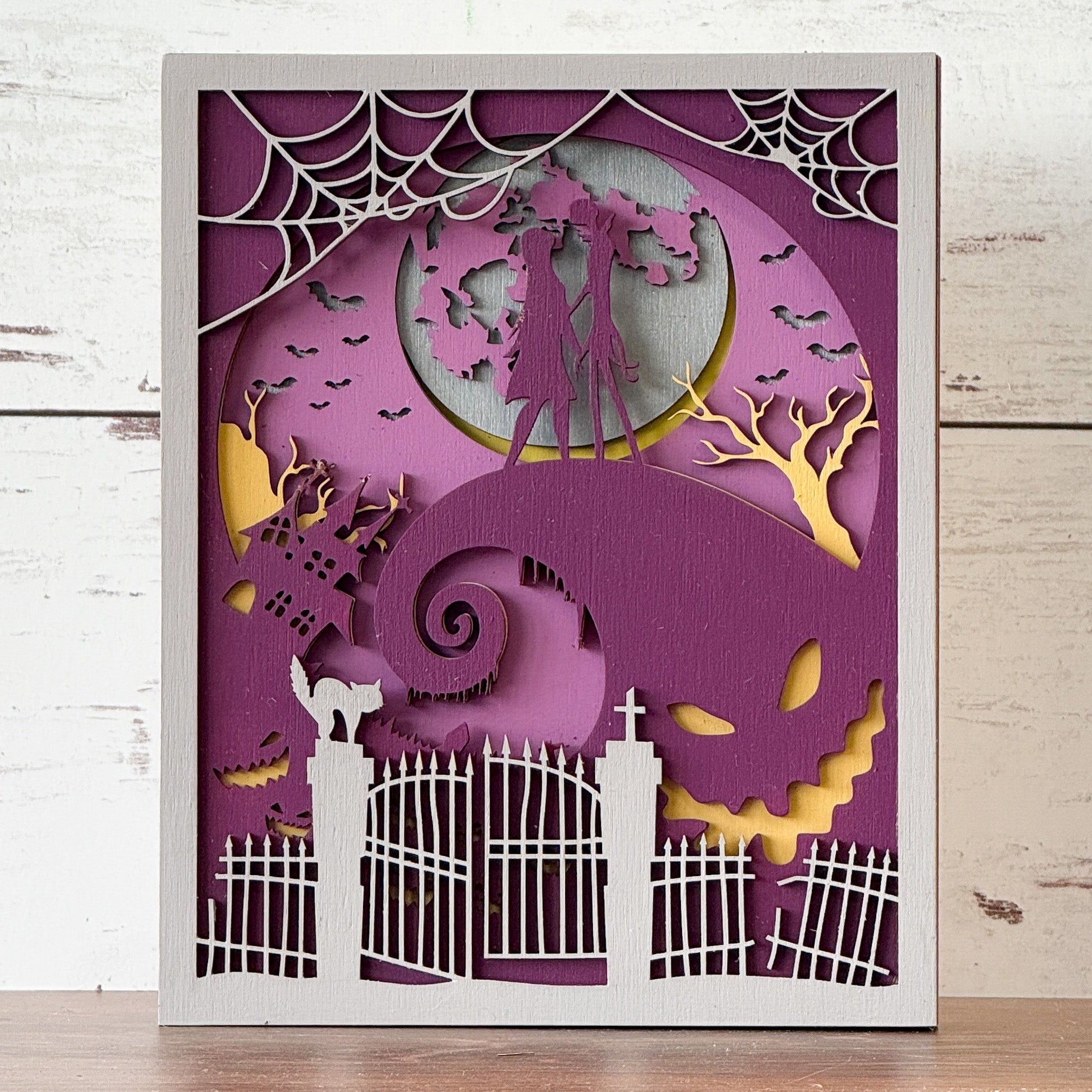 The Rustic Rhode’s “This is Halloween...Craft Night!” is a layered paper art scene featuring two figures on a hill, bats, trees, spiderwebs, a spooky fence, and Jack Skellington—ideal for any DIY Halloween craft workshop.