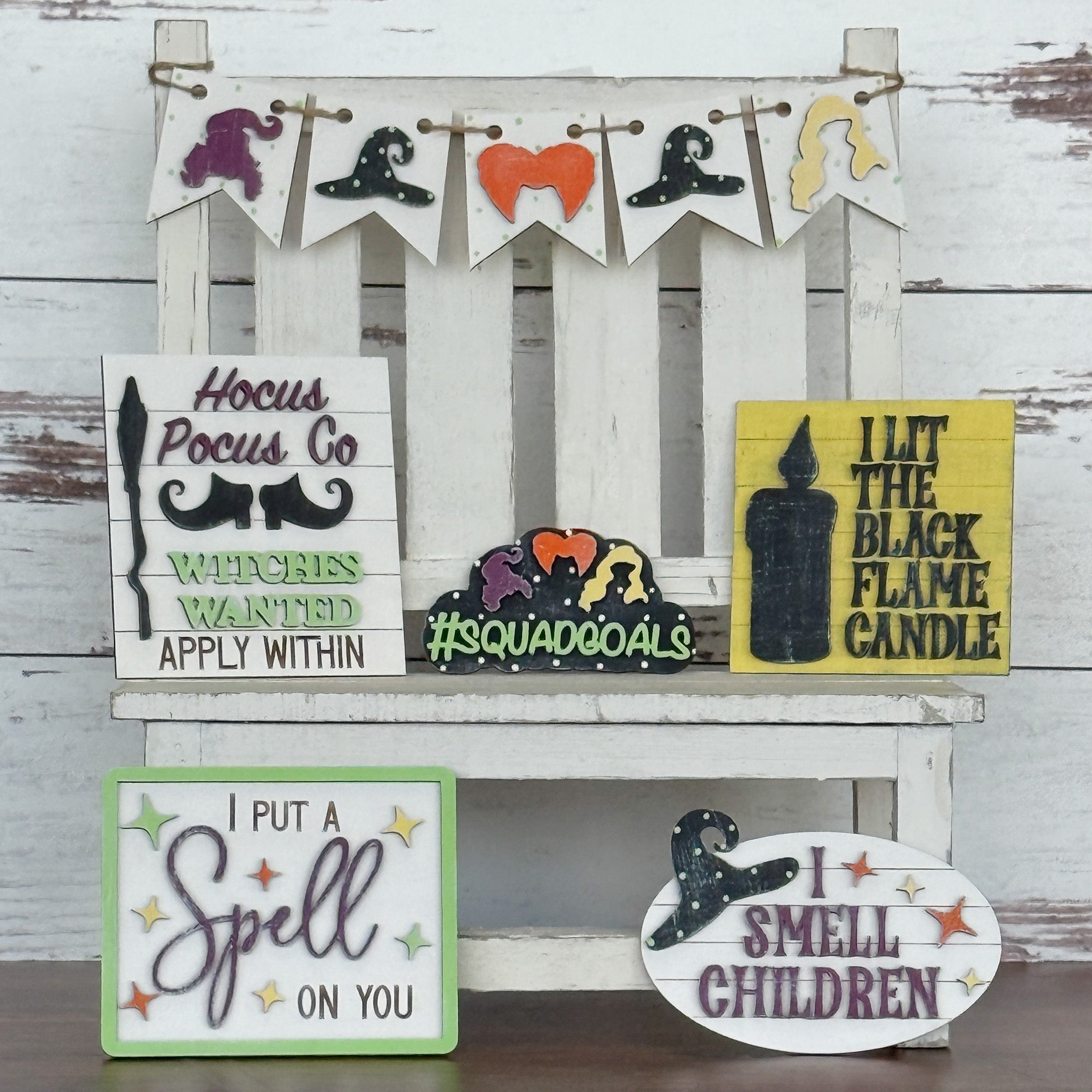 A white wooden chair displays Halloween signs from The Rustic Rhode's Hocus Pocus Craftus Workshop, featuring witch hats, candles, and phrases like Hocus Pocus Co., #Squadgoals, I put a spell on you, and I smell children.