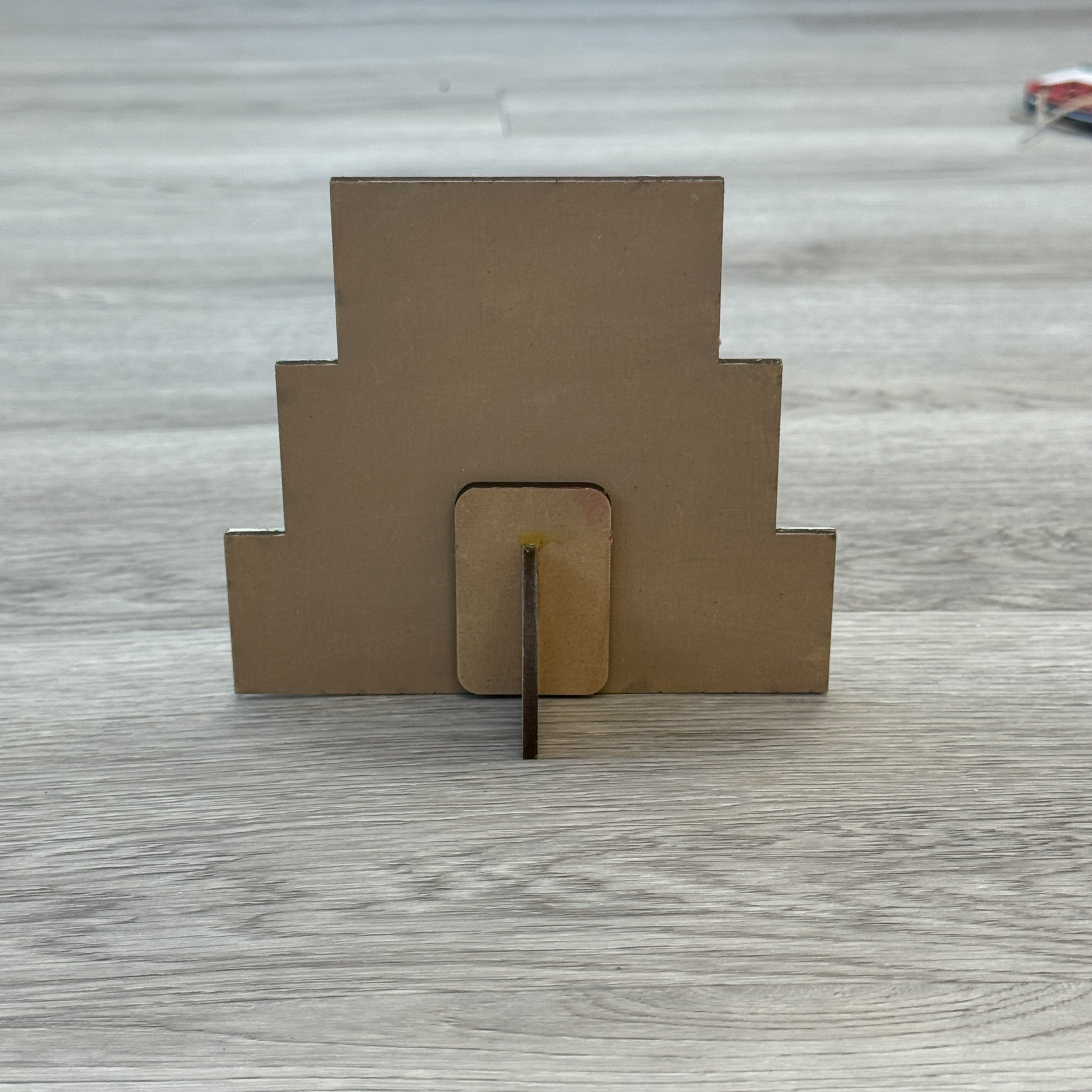 The Rustic Rhode DIY North Pole Santa Word Stacker is a stepped brown wooden decor piece with a small base and support stick—ideal for your next holiday craft kit project.