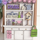 The Rustic Rhode P. Fallon Group is a miniature wooden hutch adorned with spring florals, a watering can, birdhouse, and cheerful signs—perfect for farmhouse-inspired décor or your seasonal project menu.