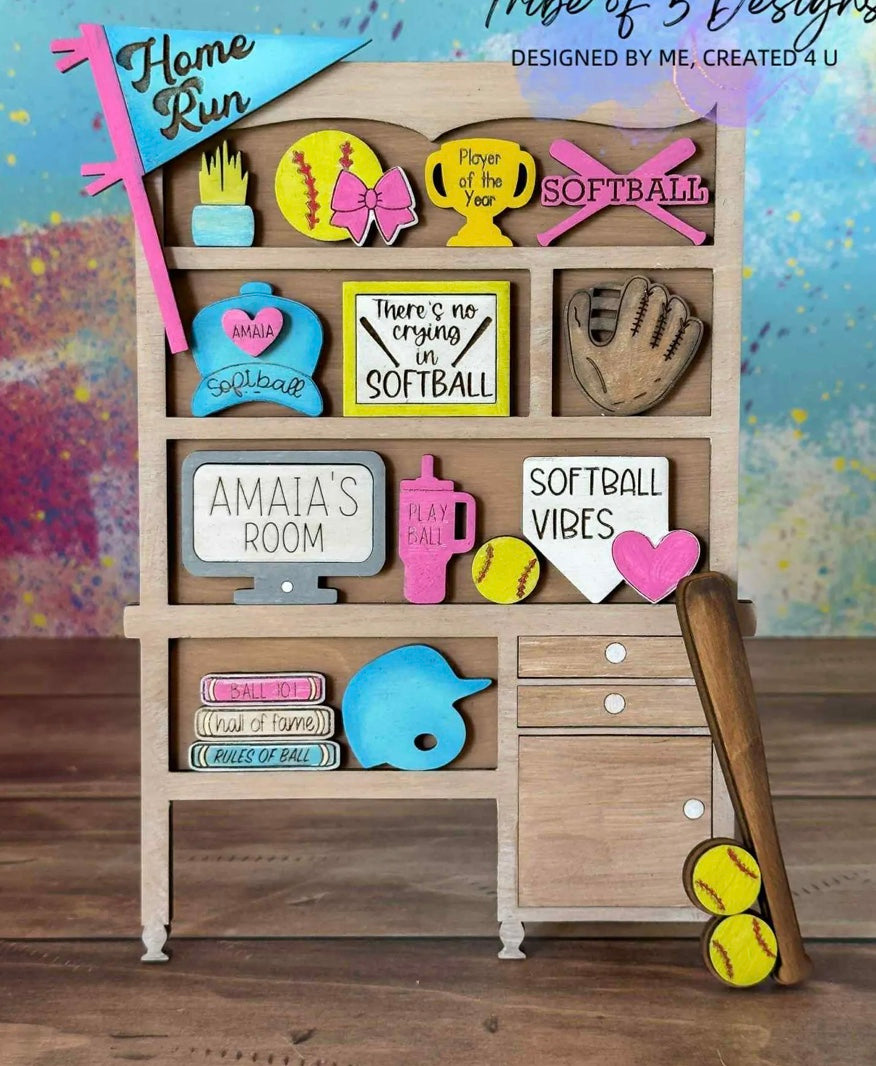 A wooden shelf featuring The Rustic Rhode’s Warwick Softball Fundraiser-10/2/25 door hangers, colorful softball-themed signs, trophies, a glove and bat with softballs, plus phrases like “Home Run” and “There’s no crying in softball.”.