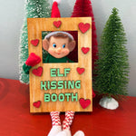 Create a charming holiday display with The Rustic Rhode DIY Elf Prop Kit—featuring a festive elf doll in a wooden Elf Kissing Booth with red heart accents and three mini Christmas trees, perfect for your Christmas décor.