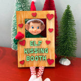 Create a charming holiday display with The Rustic Rhode DIY Elf Prop Kit—featuring a festive elf doll in a wooden Elf Kissing Booth with red heart accents and three mini Christmas trees, perfect for your Christmas décor.