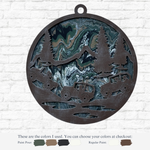 The Rustic Rhode’s DIY Paint Pour – Off Road Mountain features a round metal ornament with cut-out trees, mountains, and off-road vehicles over a swirled green, blue, black, and cream background—ideal for your next craft project. Color details below.