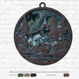 The Rustic Rhode’s DIY Paint Pour – Off Road Mountain features a round metal ornament with cut-out trees, mountains, and off-road vehicles over a swirled green, blue, black, and cream background—ideal for your next craft project. Color details below.