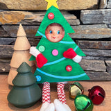 The Rustic Rhode’s DIY Elf Prop Kit features a doll dressed as a Christmas tree beside stacked stones, wooden and green tree decorations, and jingle bells—perfect for creative holiday displays or pairing with handcrafted elf props.